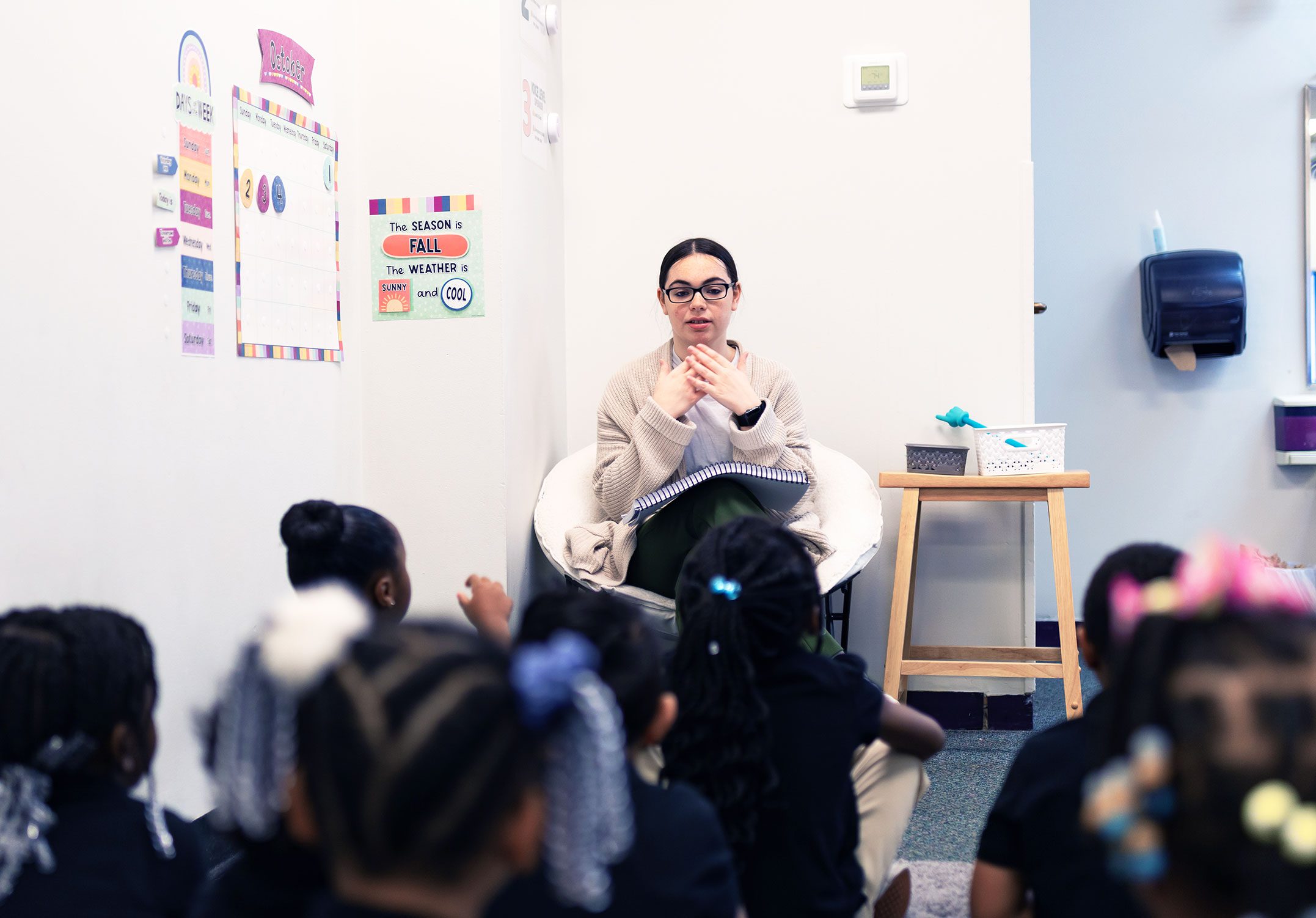 Teacher leading a group of young students seated on a classroom floor.