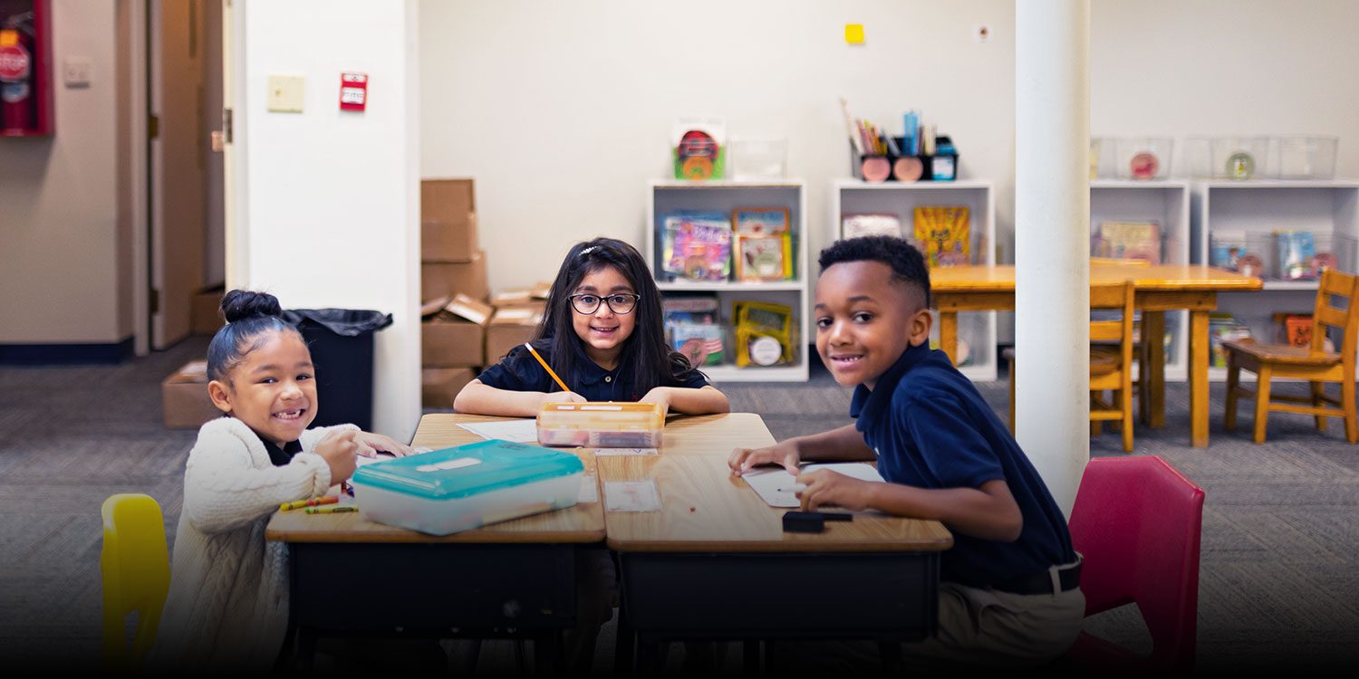 Three smiling students working at their classroom desks.