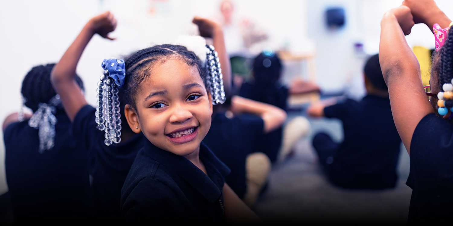Smiling student in a classroom with classmates in the background.